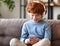 Delighted redhead boy with smartphone sitting on sofa