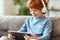 Delighted redhead boy with tablet sitting on sofa