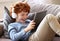 Delighted redhead boy with tablet sitting on sofa