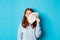 Delighted redhead woman showing money near face, smiling satisfied, standing ready for shopping over blue background