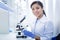 Delighted smart woman sitting in front of the microscope