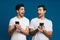 Delighted two guys expressing surprise while posing with smartphones
