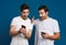 Delighted two guys expressing surprise while posing with smartphones