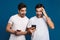 Delighted two guys expressing surprise while posing with smartphones