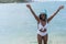 Delighted young female in swimwear smiling and raising arms while splashing clean seawater on summer weekend day