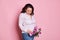 Delightful pregnant woman with tulips, smiling touching her tummy, enjoying first baby kicks,  pink background