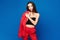 Delightful slim female model with perfect makeup and figure wearing stylish red suit standing against a blue background