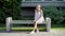 The delightful young woman sits on a bench wearing white lace dress in summertime, thinks and enjoys being alone