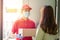 Deliver man wearing face mask in red uniform handing a parcel box over to a customer in front of the house. Postman and express
