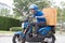 Delivery boy on motorcycle with trunk parcel box driving to fast in rush. Courier delivering order online.