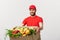 Delivery Concept: Handsome Caucasian grocery delivery courier man in red uniform with grocery box with fresh fruit and