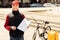 Delivery Guy Holding Folder With Paper Standing With Bike Outdoors
