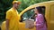 Delivery guy in yellow uniform gives parcel to female customer near car