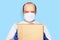 Delivery man employee face mask gloves hold mockup cardboard box isolated on blue.