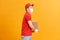 Delivery man employee in red cap blank t-shirt uniform face mask gloves hold cardboard box isolated on yellow background