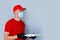 Delivery man employee in red cap blank t-shirt uniform face mask gloves hold  cardboard box pizza isolated on grey background