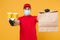 Delivery man guy employee in red cap uniform mask gloves hold craft paper packet with food coffee isolated on yellow