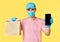 Delivery man hold paper packet with food and smartphone wearing face mask and gloves as protection for COVID-19