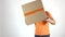 Delivery man in orange uniform throwing a big parcel at the camera. Light gray backround, slow motion studio shot