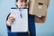 Delivery man in uniform is holding parcel cardboard box over blue background.