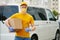 Delivery Man in yellow uniform medical mask and gloves holds a package. Safety delivery service covid-19 pandemic