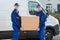 Delivery Men Carrying Cardboard Box Against Truck