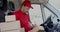 Delivery service man sitting in van and writing documents on clipboard before delivering a package to customer