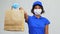 Delivery woman in mask holding paper bag with food