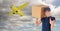 Delivery woman showing thumbs up while carrying parcel against airplane flying in sky