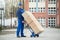 Deliveryman Holding Trolley Loaded With Cardboard Boxes