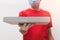 Deliveryman wearing red t-shirt, protective gloves and mask holding pizza box close-up.