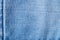 Denim background texture. Close-up of details of empty light blue jeans fabric jean surface with dark blue vertical seam on left