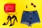 Denim shorts, black shoes, red handbag and glasses. Bright yellow background. Fashionable concept