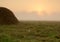 Dense morning fog over the meadow and haystack just after sunri