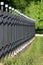 Dense row of wrought iron fence made of vertical metal poles with wrought iron cube on top mounted on concrete foundation