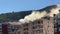 Dense smoke from a fire in a high-rise building rises above the roof at the foot of the mountains