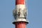 Densely installed multiple cell phone antennas and transmitters on tall white and red industrial chimney surrounded with metal