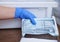 Dentist in blue latex gloves is taking a sealed dental stainless steel instrument from an autoclave sterilizer