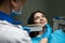 Dentist in blue medical gloves and mask applying sample from tooth enamel scale to woman patient teeth to choose right shade for