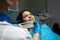 Dentist in blue medical gloves and mask applying sample from tooth enamel scale to woman patient teeth to pick up right shade for