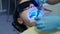 Dentist is fixing woman's veneers and crowns using UV lamp in dentistry clinic.