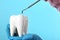 Dentist holding ceramic model of tooth and professional tool on color background