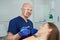 A dentist holds a dental mirror and a drill near a patient in the dental chair