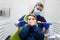 Dentist holds electric brush and mirror near boy`s mouth. Teen doesn`t want to do oral hygiene. Pediatric dentistry concept.