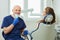 Dentist lowered medical face mask and smiles, holds a dental drill near patient