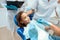 A dentist is preparing to treat the teeth of a little girl. There are nurses around. Girl smiling