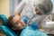 Dentist woman doing teeth checkup of little girl looking with fear in a dental chair