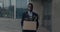 Depressed african american male office worker leaving business center building with box of personal stuff