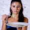 Depressed dieting woman holding folk looking at small green vegetable on empty plate