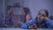 Depressed girl sitting behind rainy window, parents quarrelling on background